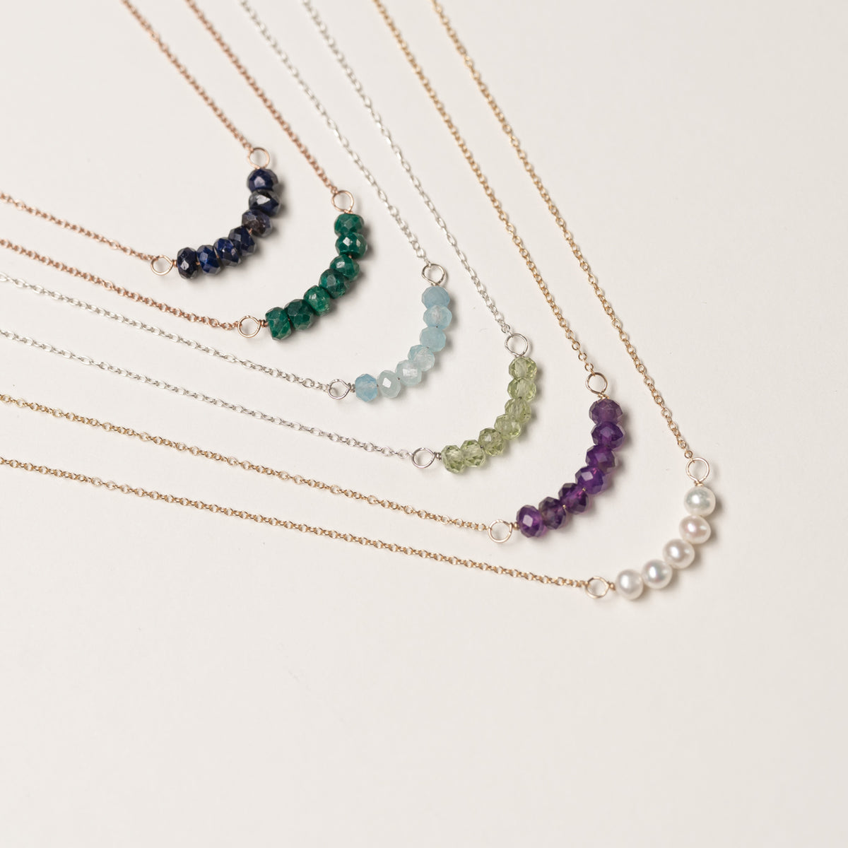 Mixed metal gemstone and pearl necklaces arranged on a neutral background